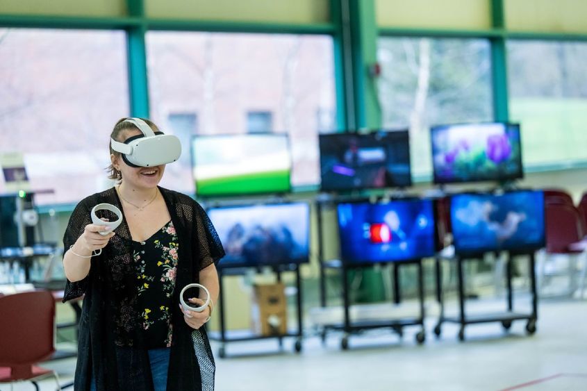 A woman experiments with VR while wearing a headset and holding two controllers.