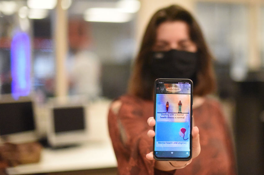 A woman holds up a smartphone with a mental-health app on the screen.
