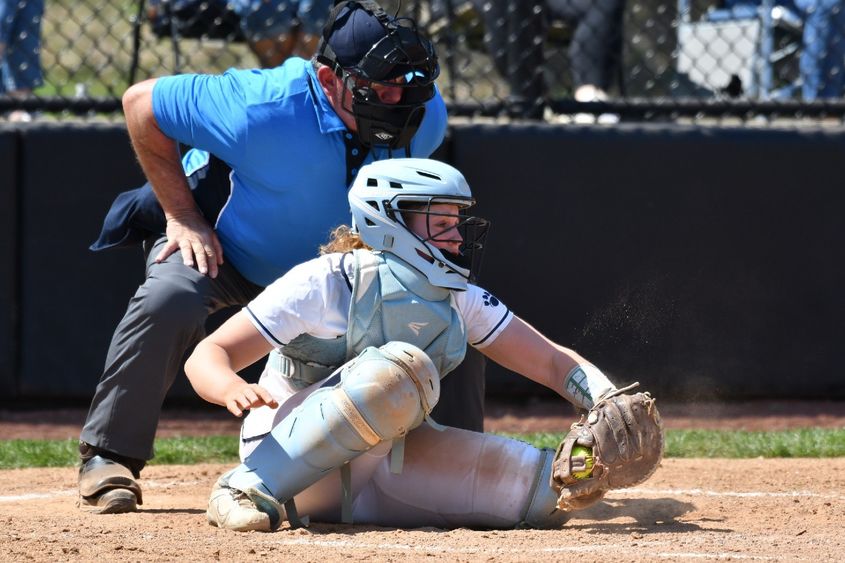 A catcher for the Penn State Behrend softball team grabs the ball as the umpire leans over her shoulder.