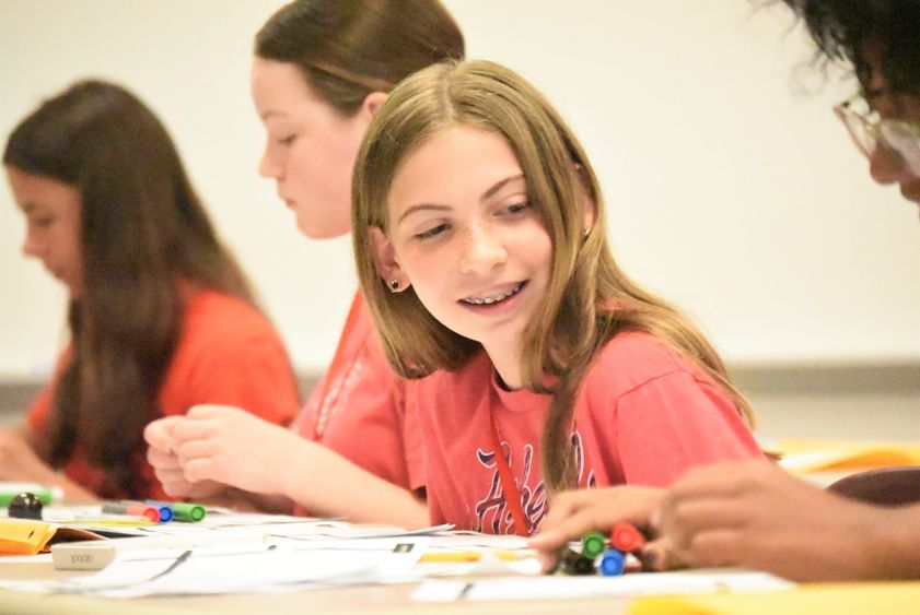 A middle-schooler looks to her side and smiles as a classmate works on a drawing project.