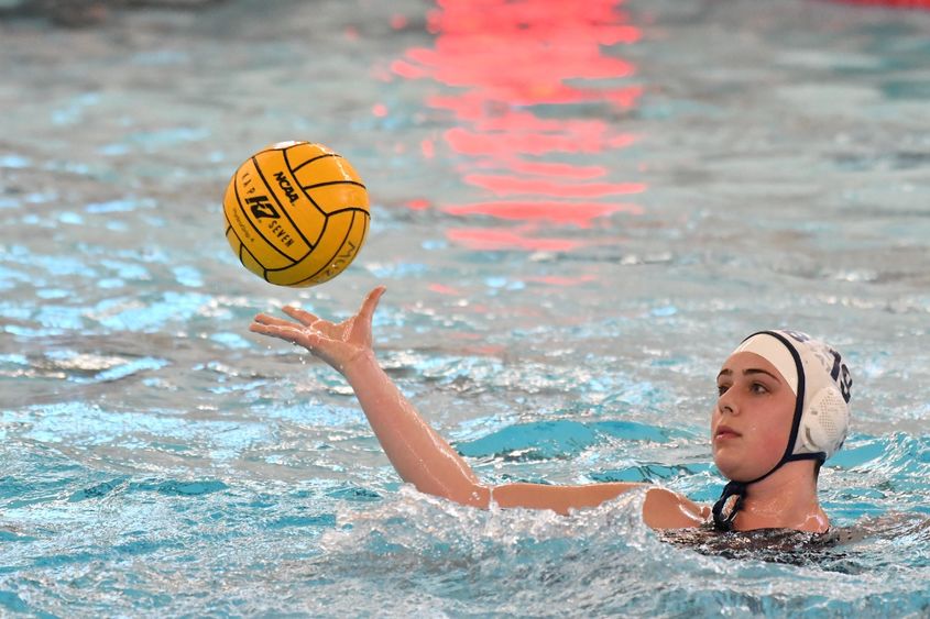 A female water polo player catches the ball while treading water.