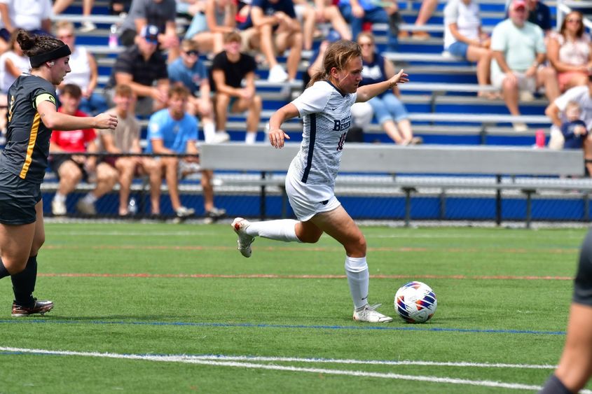 A female Penn State Behrend soccer player advances with the ball.