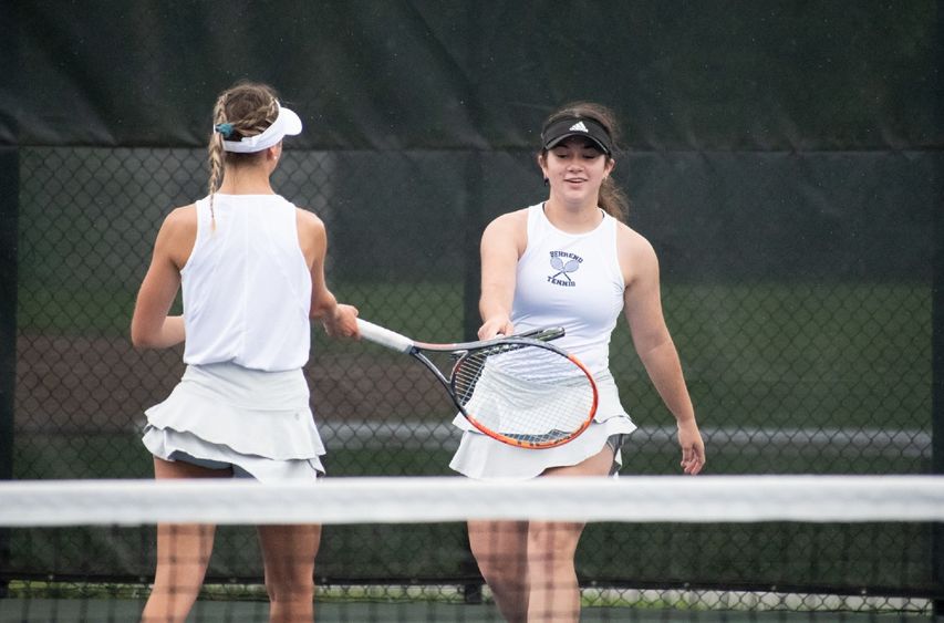 Two Penn State Behrend tennis players touch rackets after scoring a point.