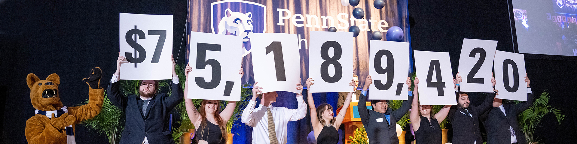 The Nittany Lion presents students holding number signs reading $75,189,420, Penn State Behrend's campaign fundraising total, at the college's Glenhill Appreciation Dinner in 2022.