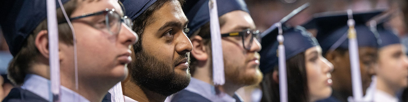 Student graduates sitting in caps and gowns at commencement ceremony