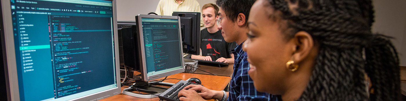 A professor at Penn State Behrend advises three students working on computer code.