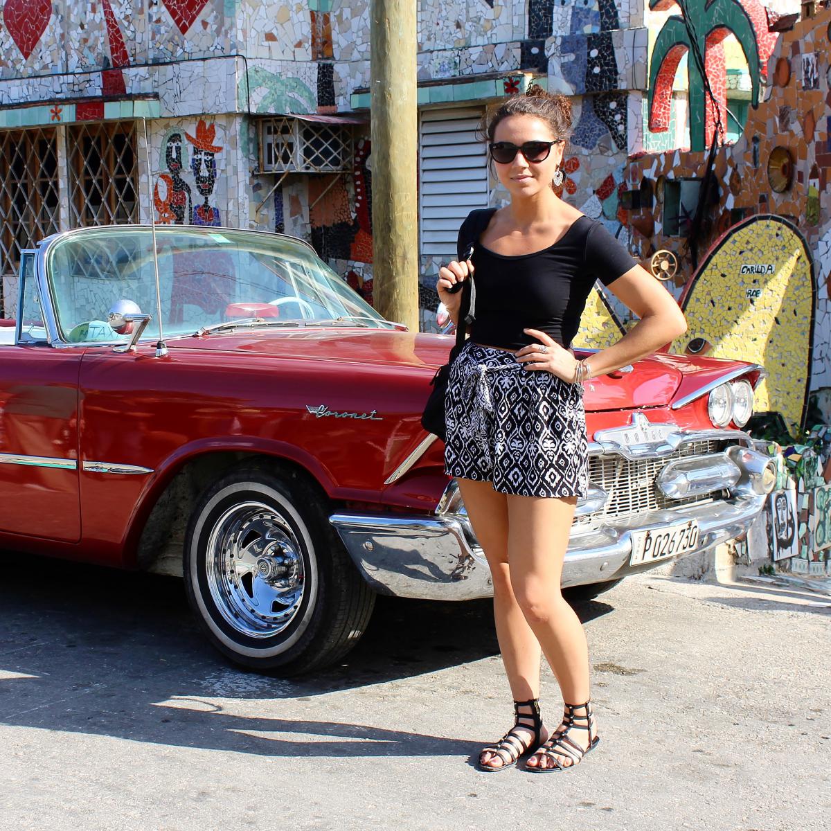 A Penn State Behrend student stands near an old car in Cuba.