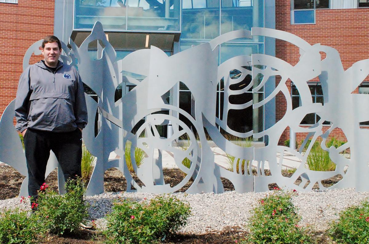 Penn State Behrend senior Will Gerould stands near an outdoor sculpture.