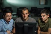 A professor and two students work on a computer.